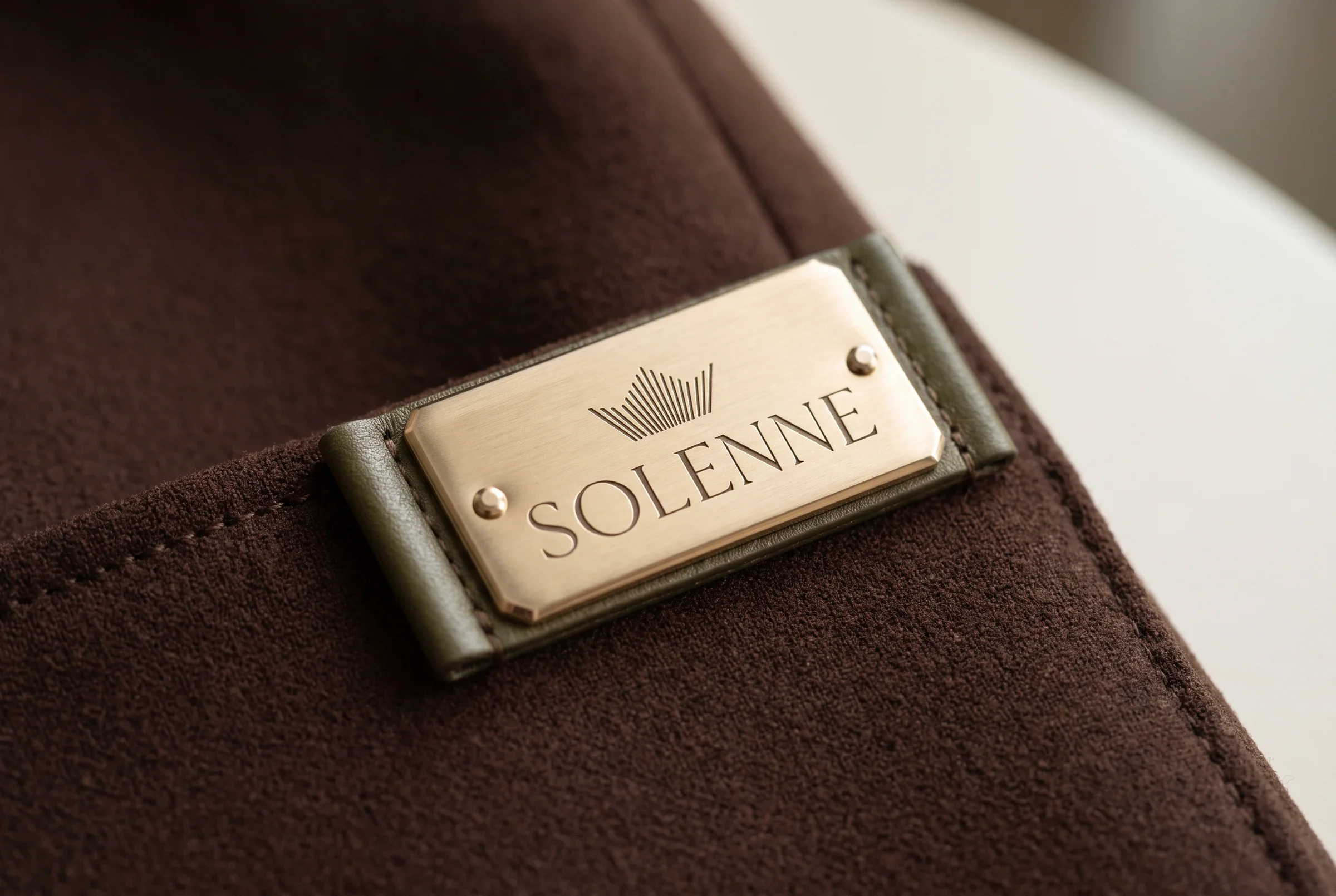 Brushed metal Solenne plaque stitched onto a brown garment.